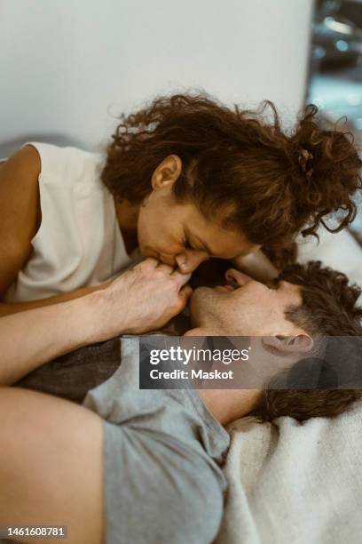 girlfriend kissing boyfriend's hand lying on bed at home - pareja de mediana edad fotografías e imágenes de stock