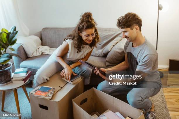 man sharing photo frame with girlfriend while unboxing cardboard boxes at home - memory box stock pictures, royalty-free photos & images