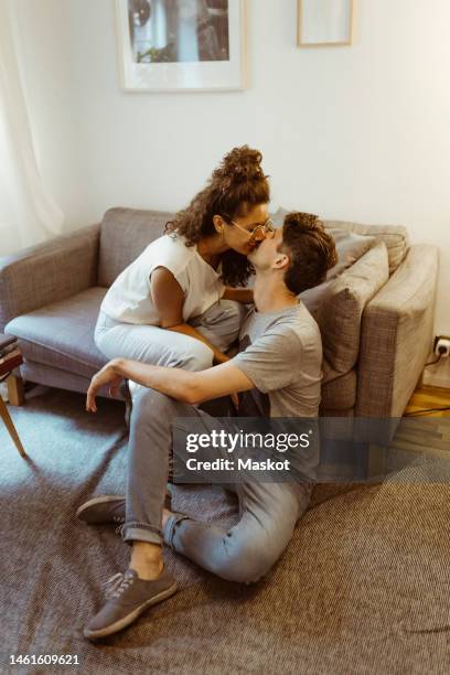 romantic boyfriend and girlfriend kissing each other sitting in living room at home - ic foto e immagini stock