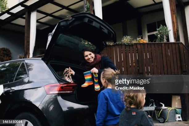 happy mother with daughters loading boots and bag in trunk of electric car - family car at home stock-fotos und bilder