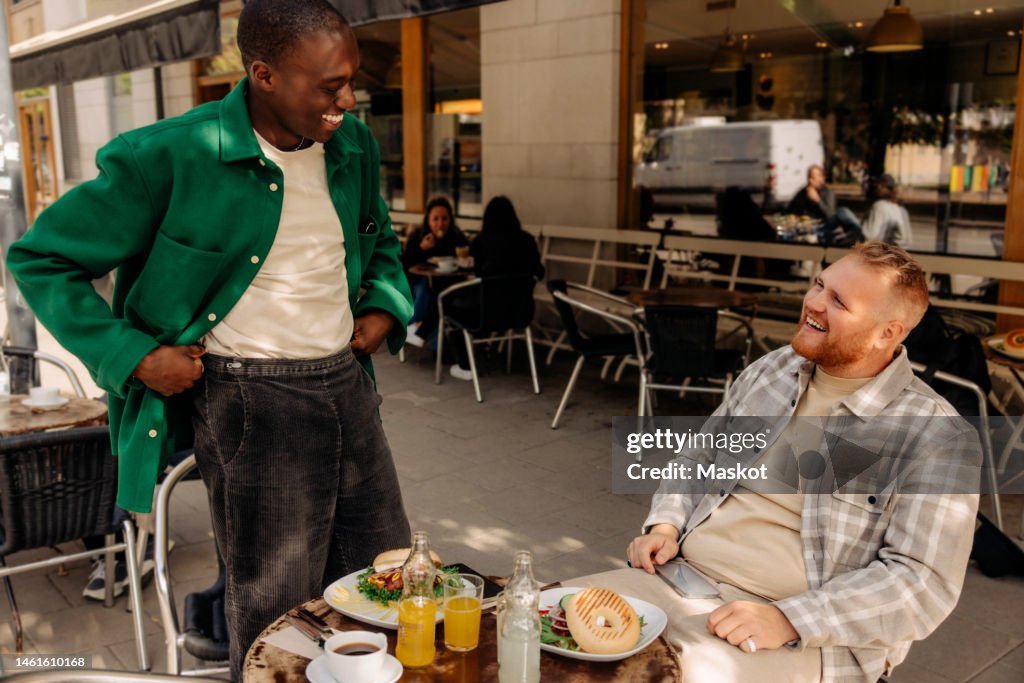 Happy multiracial male friends talking to each other at sidewalk cafe