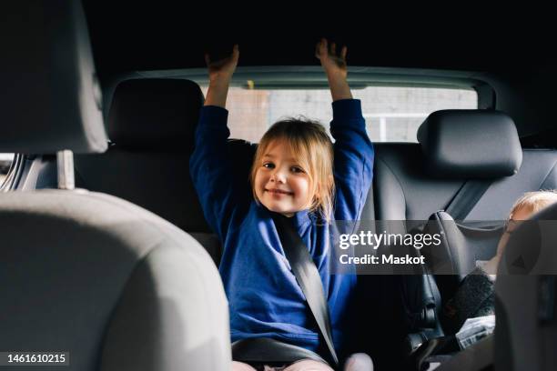portrait of smiling girl with arms raised sitting at back seat in car - car back seat stock pictures, royalty-free photos & images