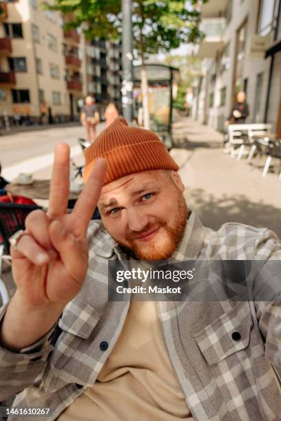 portrait of smiling man showing peace sign while taking selfie - victory sign stock-fotos und bilder