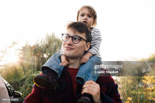 smiling father wearing eyeglasses carrying daughter on shoulder - carrying on shoulders stock pictures, royalty-free photos & images