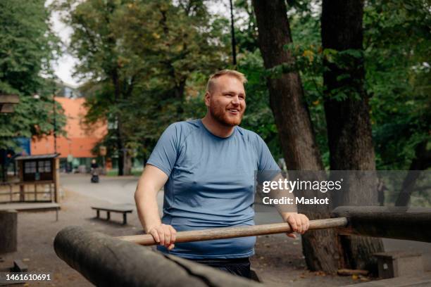 smiling overweight man exercising while standing at park - obesity concept stock pictures, royalty-free photos & images