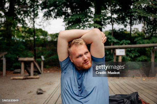 obese man looking away while doing stretching at park - heavy stock pictures, royalty-free photos & images