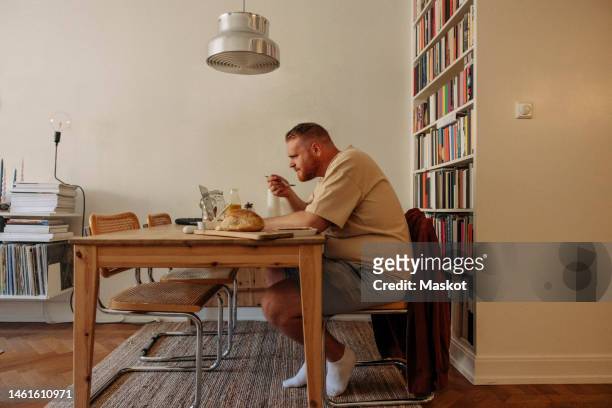 side view of overweight man having breakfast while watching laptop at table in home - obesity icon stock pictures, royalty-free photos & images
