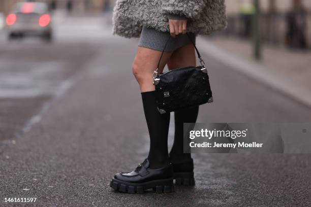 Sonia Lyson seen wearing Louis Vuitton black leather logo pattern bag, Prada black shiny leather loafer, Wolford black transparent socks, Edited grey...