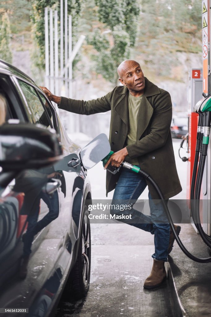 Mature man looking away while refueling car standing at gas station