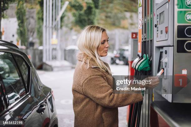 mature woman doing payment via credit card at fuel station - petrol paying stock-fotos und bilder