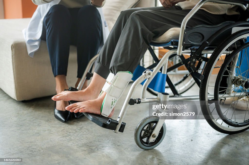 Women broken feet with a plastic boot ankle brace injury protecting boot while sitting on wheelchair at the hospital