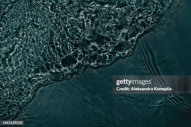 dark gray transparent clear water surface texture with ripples, splashes and waves in sunlight. - viernes fotografías e imágenes de stock