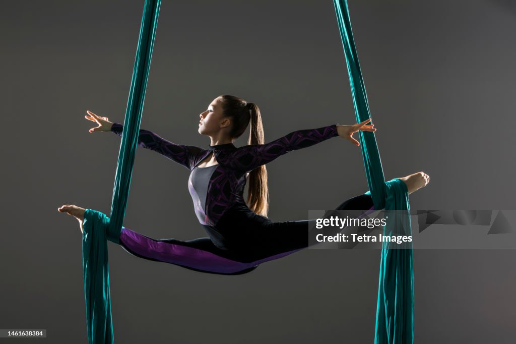 Young acrobat doing splits on aerial silks