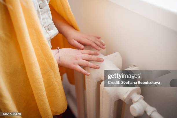 child warms his hands on the heater radiator - heizung stock-fotos und bilder