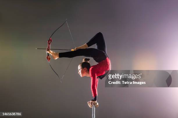 young acrobat performing with archery bow on gymnastics bar - luftakrobat stock-fotos und bilder
