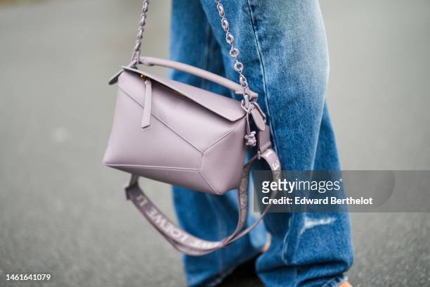 Guest wears a pale purple shiny leather Puzzle shoulder bag from Loewe, blue denim faded large pants, outside Selam Fessahaye, during the Copenhagen...