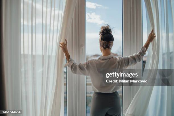 eine junge frau öffnet morgens bei sonnenaufgang die vorhänge im zimmer - curtain hotel stock-fotos und bilder