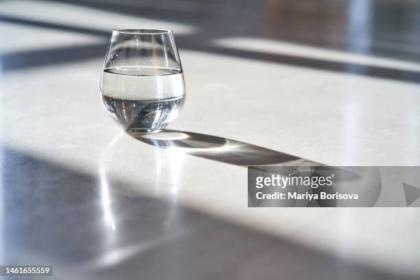 a glass of water stands on a white marble floor in the rays of the bright sun. - crystal glasses stock pictures, royalty-free photos & images