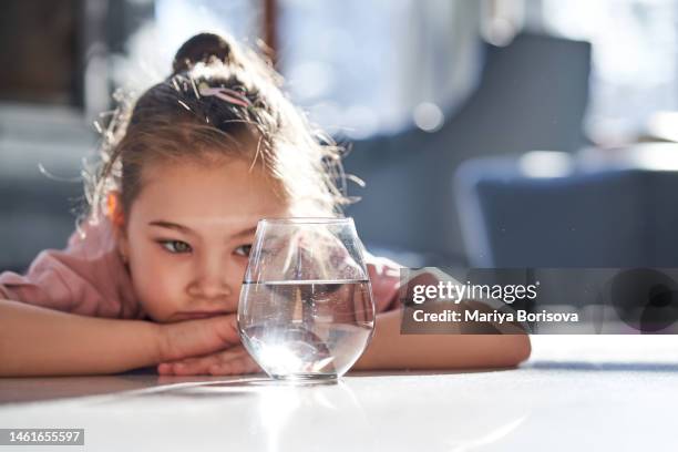 a girl in pink clothes lies on a marble floor and looks at a glass of water. - beaten up stockfoto's en -beelden