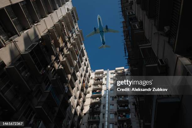 a passenger plane flies low over a house or building in a residential area. bottom view. the plane is on the background of a blue cloudless sky, landing or taking off near the city. tourist destinations. - jumbo hostel stock pictures, royalty-free photos & images