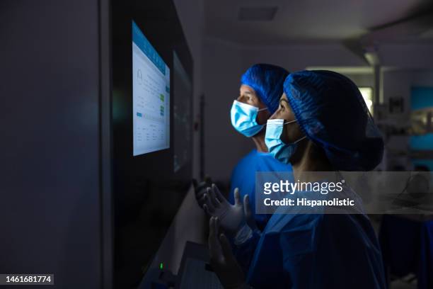 ärzte, die sich die medizinischen testergebnisse auf dem monitor im operationssaal ansehen - medical technology stock-fotos und bilder