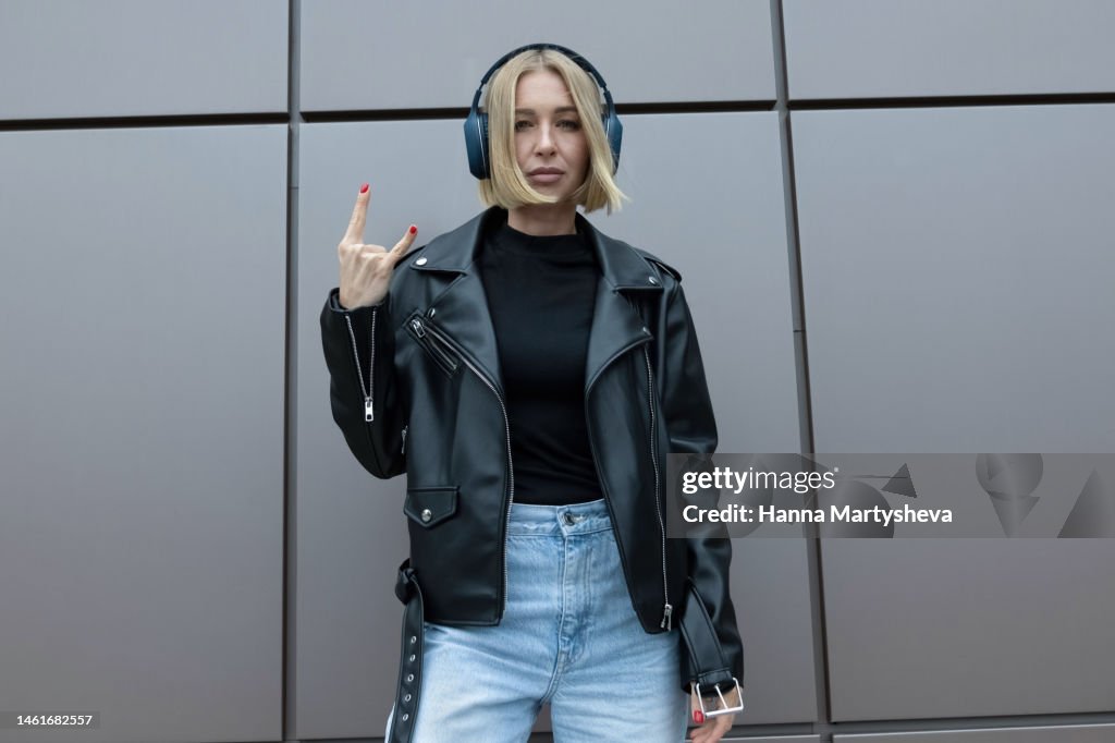 Fashionable woman with headphones in front of city wall