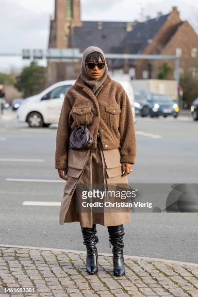 Loicka Grace wears balaclava, brown fleece jacket, skirt with side pockets, black boots, brown bag, sunglasses outside OpéraSport during the...