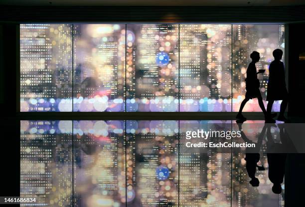 people in silhouette passing giant led screen with skyline of new york at night - 通過する ストックフォトと画像