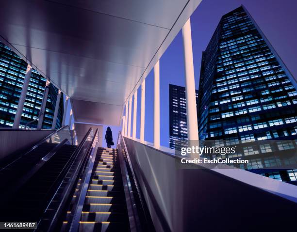 businesswoman on top of moving escalator at modern illuminated business district - finanzviertel stock-fotos und bilder