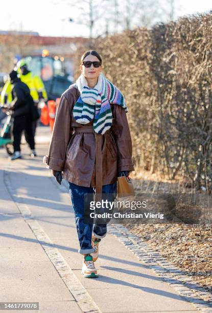 Julia Haghjoo wears brown belted leather jacket, striped knit over shoulders, denim jeans, black gloves, brown bag, sneaker outside Munthe during the...