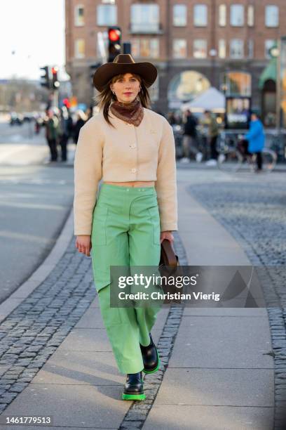 Guest wears brown cowboy hat, beige cropped jacket, green pants, brown bag, black green boots outside Mark Kenly Domino Tan during the Copenhagen...