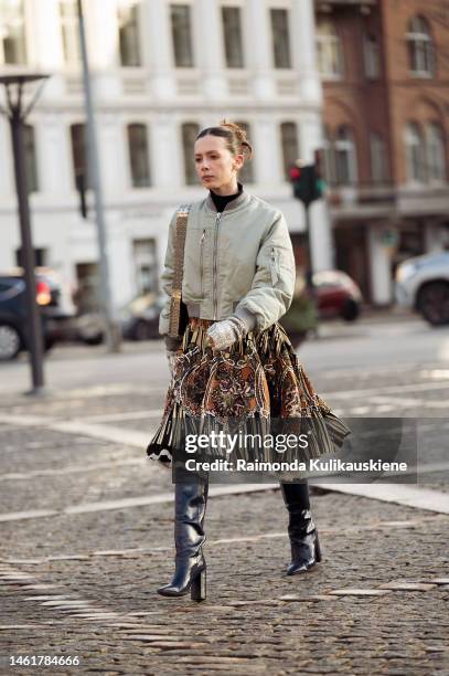 Candice Burgi wears a black wool turtleneck pullover, a pale khaki zipper bomber jacket, a gold shiny 1969 Nano metal-disc shoulder bag from Paco...