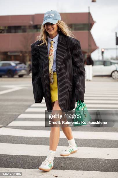 Emili Sindlev wearing a blue with embroidered white words New York denim cap, a pale blue with white stripes shirt, a tie with yellow, orange, green,...