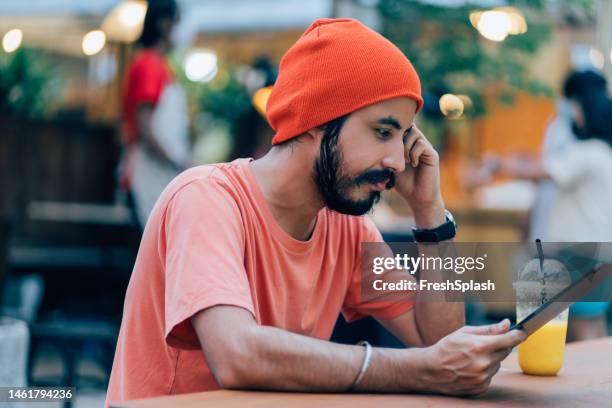 a serious businessman watching something on his tablet while sitting outdoors - pensive indian man stock pictures, royalty-free photos & images