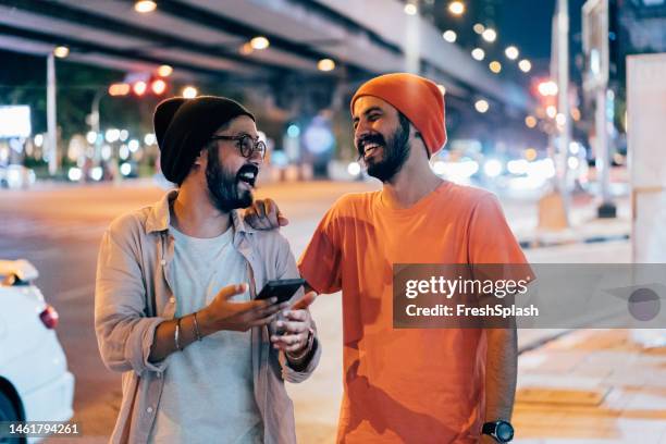 zwei glückliche freunde, die ihr handy benutzen und lachen, während sie nachts auf der straße stehen - cell mates stock-fotos und bilder
