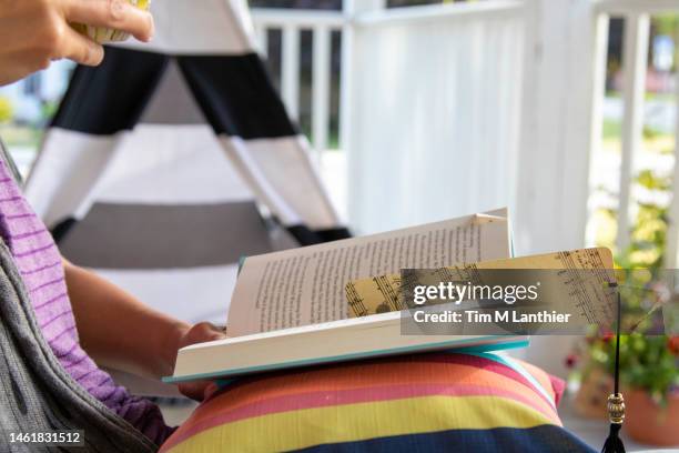 woman reading a book on front porch in summer - segnalibro foto e immagini stock