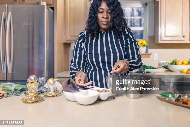 nella sua cucina, una donna afroamericana matura prepara una tisana. - "alex potemkin" or "krakozawr" foto e immagini stock