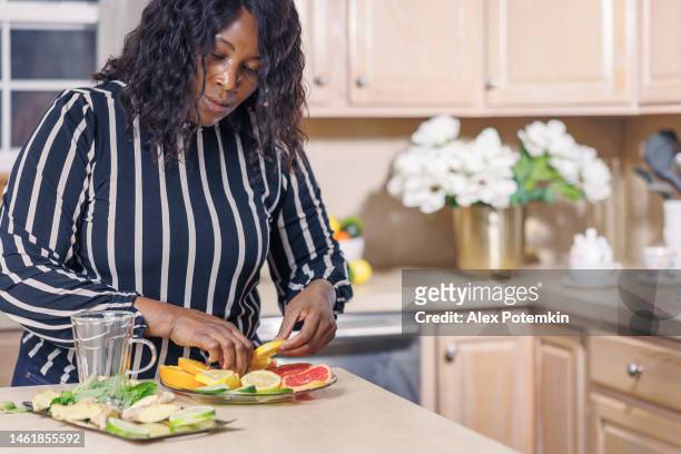 è una donna afroamericana nera matura e attraente che sta preparando tisane nella sua cucina mentre organizza il lato frutta. - "alex potemkin" or "krakozawr" foto e immagini stock