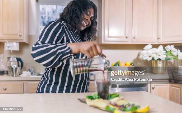 una donna afroamericana nera matura e attraente sta preparando una tisana nella sua cucina. - "alex potemkin" or "krakozawr" foto e immagini stock