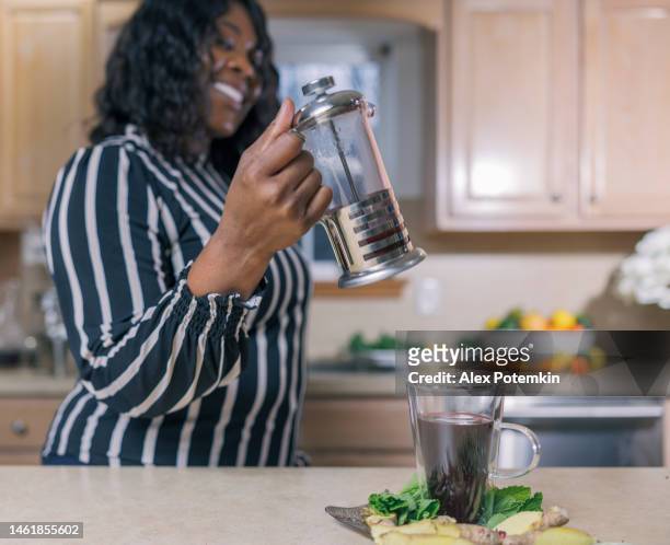 la tisana è fatta da una donna afroamericana nera matura e attraente nella sua cucina. messa a fuoco selettiva in primo piano. - "alex potemkin" or "krakozawr" foto e immagini stock