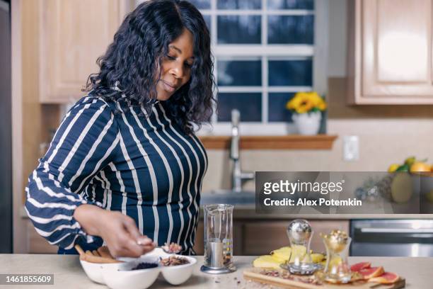 una matura e attraente donna afroamericana nera sta preparando una tisana usando una pressa francese nella sua cucina. - "alex potemkin" or "krakozawr" foto e immagini stock