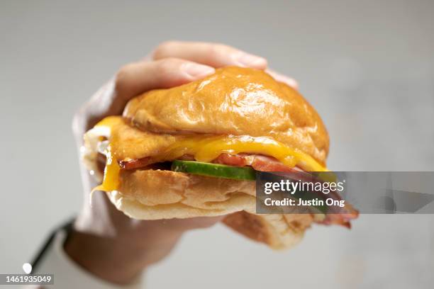 hand squeezing a burger on a brioche bun with fried egg, ham cheese, cucumbers and sauce. - hand holding burger stock pictures, royalty-free photos & images