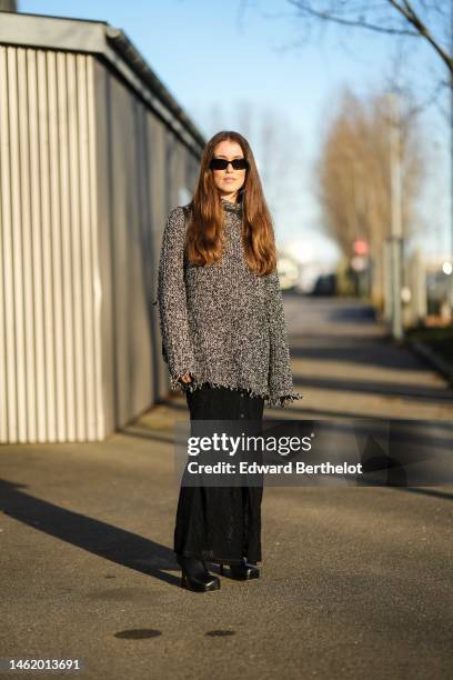 Annabel Rosendahl wears black sunglasses, a gray and white wool high neck / oversized pullover, a black shiny leather shoulder bag, black embossed...