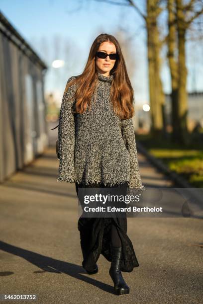 Annabel Rosendahl wears black sunglasses, a gray and white wool high neck / oversized pullover, a black shiny leather shoulder bag, black embossed...