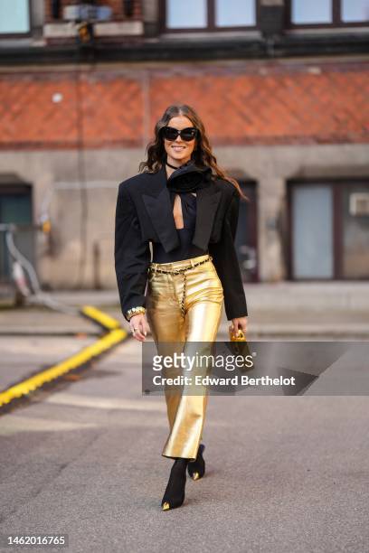 Nina Sandbech wears black sunglasses, gold earrings, a black oversized flower necklace, a black cut-out chest / halter neck body, a black...