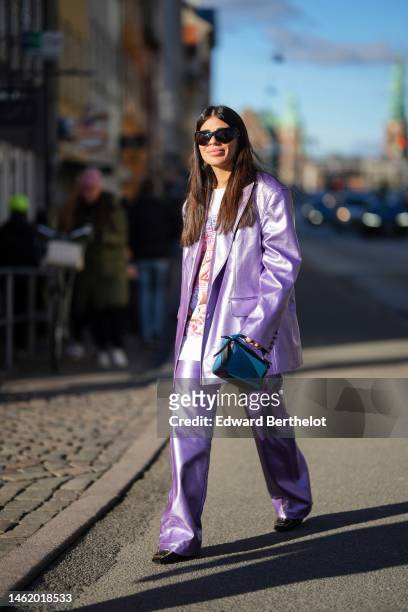 Heloïse Salessy wears black sunglasses, a white with multicolored print pattern oversized t-shirt, a silver purple shiny leather oversized blazer...