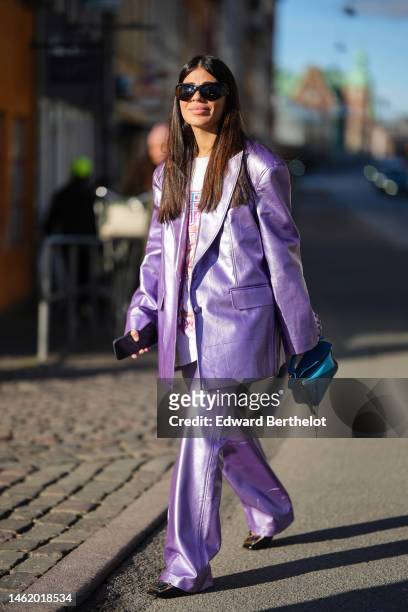 Heloïse Salessy wears black sunglasses, a white with multicolored print pattern oversized t-shirt, a silver purple shiny leather oversized blazer...
