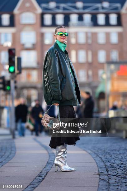 Marianne Theodorsen wears green sunglasses, white large pearls logo pendant earrings from Chanel, a green zipper high neck sweater, a dark green...