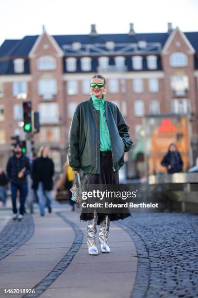 Marianne Theodorsen wears green sunglasses, white large pearls logo pendant earrings from Chanel, a green zipper high neck sweater, a dark green...