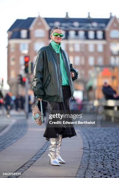 Marianne Theodorsen wears green sunglasses, white large pearls logo pendant earrings from Chanel, a green zipper high neck sweater, a dark green...